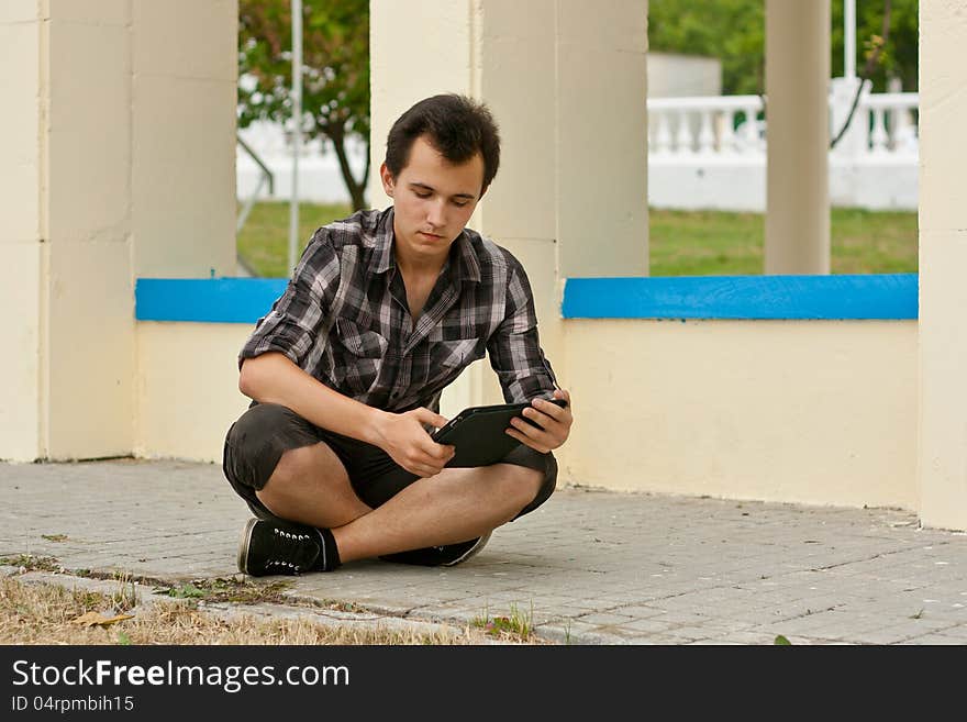 Young man sit on the sidewalk and work on the flatbed computer. Young man sit on the sidewalk and work on the flatbed computer