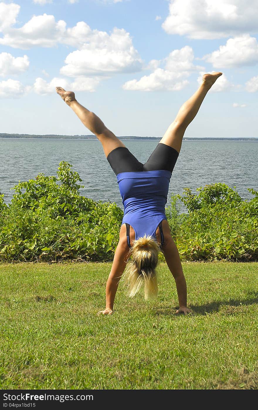 An athletic girl does a hand stand on the lawn by a lake. An athletic girl does a hand stand on the lawn by a lake.