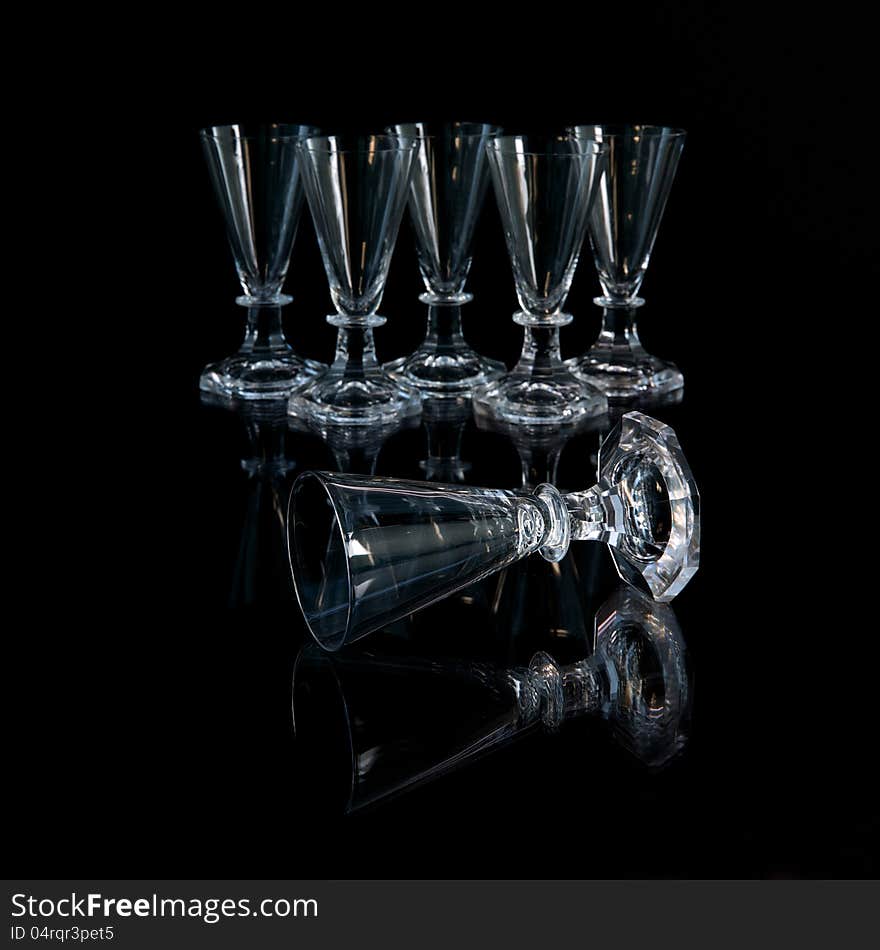 The six old crystal shot glasses where one is lying in front of the others. The six old crystal shot glasses where one is lying in front of the others.