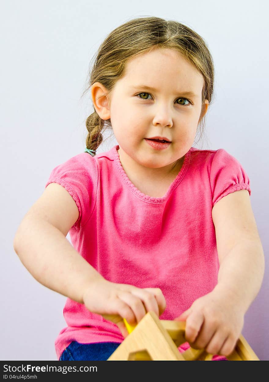 Close up of pretty three-year-old girl with braids plays with block puzzle isolated on white. Close up of pretty three-year-old girl with braids plays with block puzzle isolated on white.