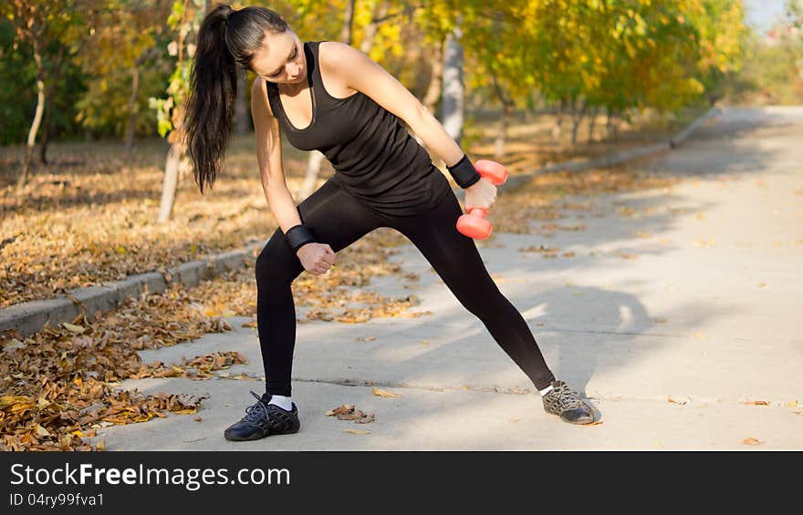 Woman in sportswear leaning forward and raising her arm to the side while working out with a dumbbell. Woman in sportswear leaning forward and raising her arm to the side while working out with a dumbbell