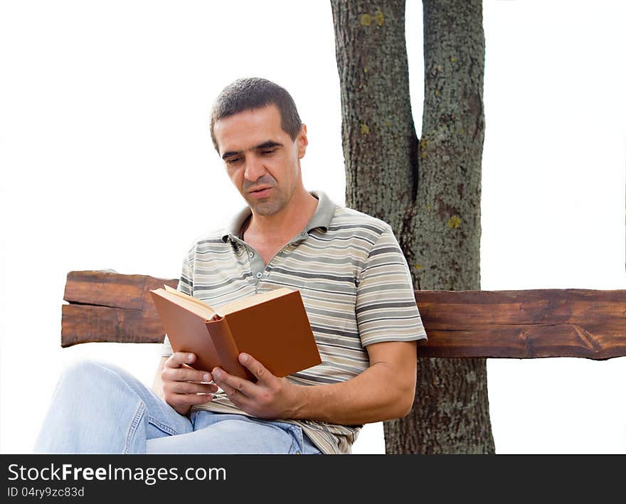 Middle-aged man reading a book sitting on a rustic wooden bench againsta tree trunk isolated on white