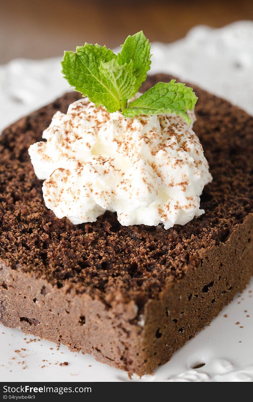 Piece of chocolate cake with whipped cream and mint on a white plate