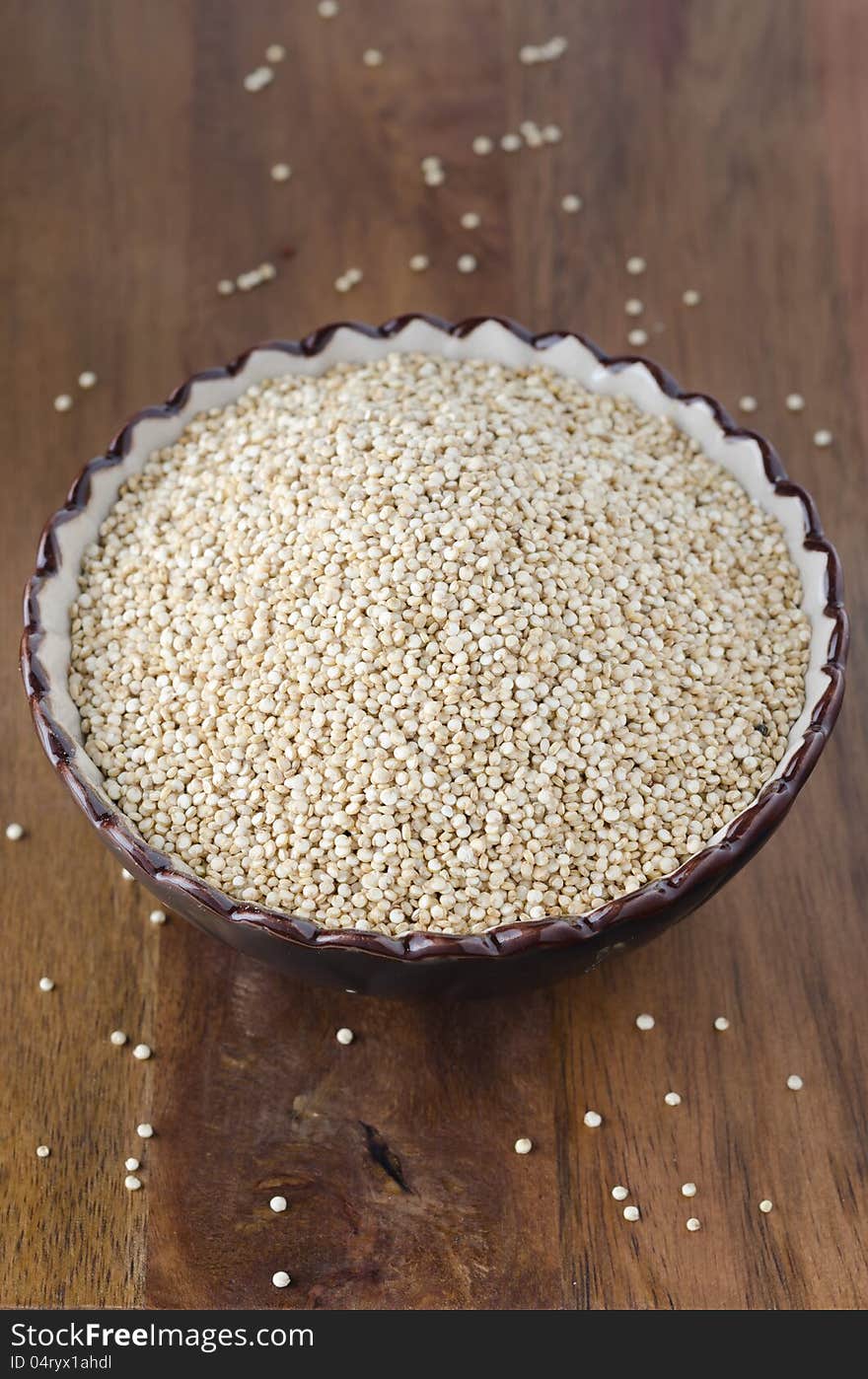 Dry grain quinoa in a ceramic bowl on wooden table