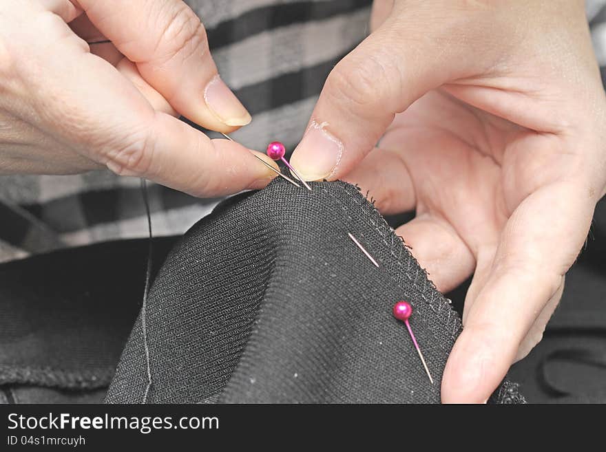 Female hands is sewing black dress. Female hands is sewing black dress