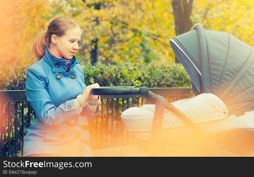 Young mother with a pram on a walk in the park in autumn. Young mother with a pram on a walk in the park in autumn