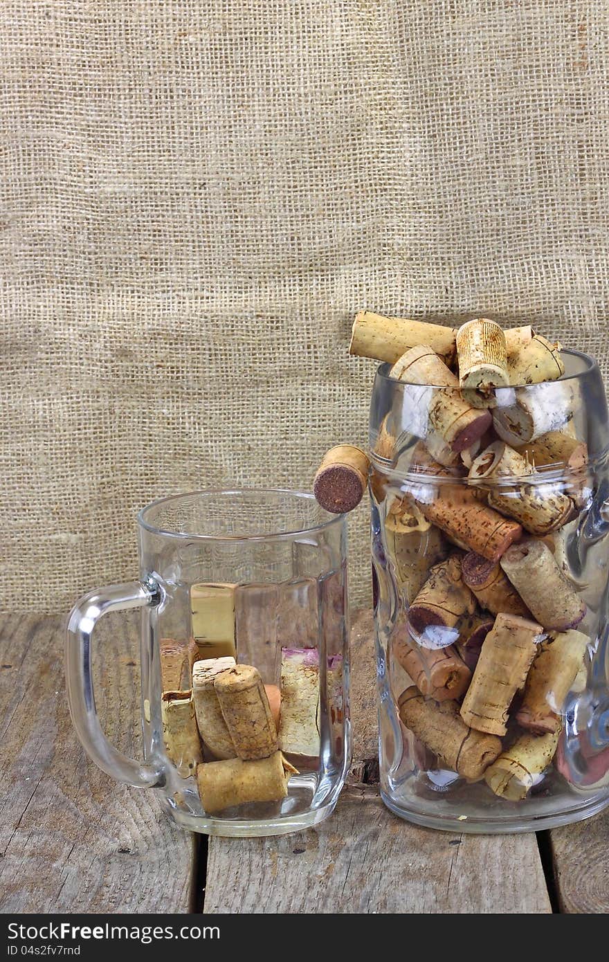 Two beer mugs filled with corks from wine bottles are on the rough wooden table. Sackcloth background. Two beer mugs filled with corks from wine bottles are on the rough wooden table. Sackcloth background