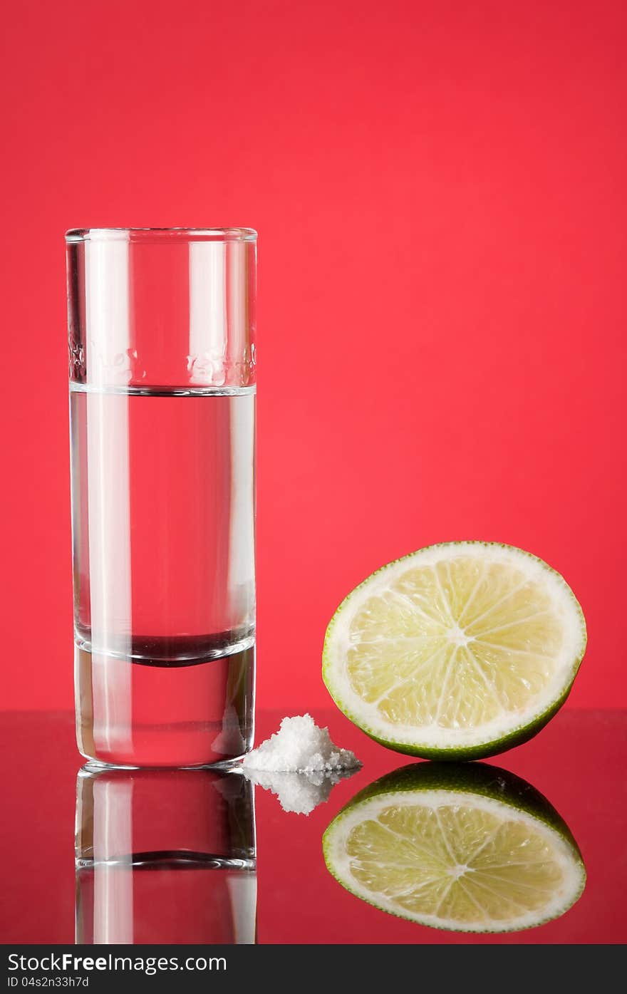 Tequila in a glass with a slice of lemon on a red background