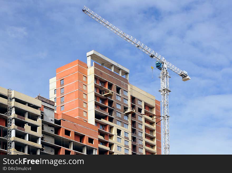 The crane and the house under construction against the sky. The crane and the house under construction against the sky