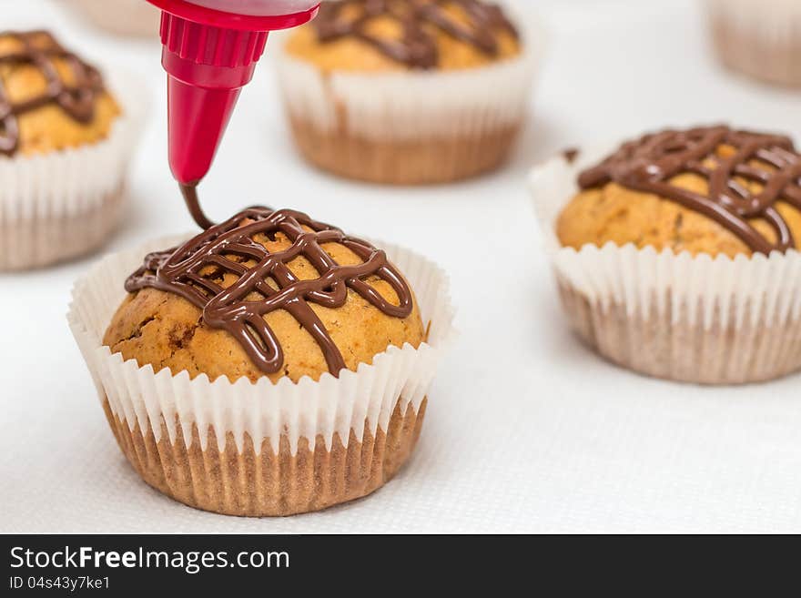 Muffins on a white paper towel getting a chocolate glaze with a decoration bag. Muffins on a white paper towel getting a chocolate glaze with a decoration bag.