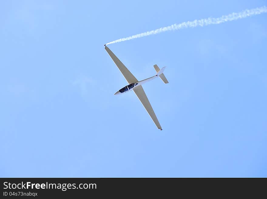 Sports glider aerobatic pilot flying in the sky with blue racing with trail of white smoke. Sports glider aerobatic pilot flying in the sky with blue racing with trail of white smoke