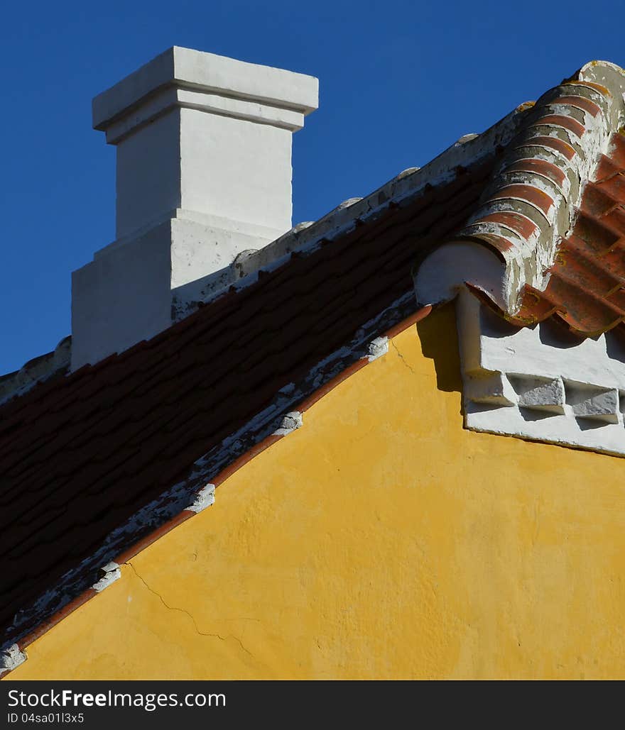 Behind the classic yellow gable, a chimney on the rooftop of red tiles is seen with the characteristic white paint decoration of Skagen, Denmark. Behind the classic yellow gable, a chimney on the rooftop of red tiles is seen with the characteristic white paint decoration of Skagen, Denmark