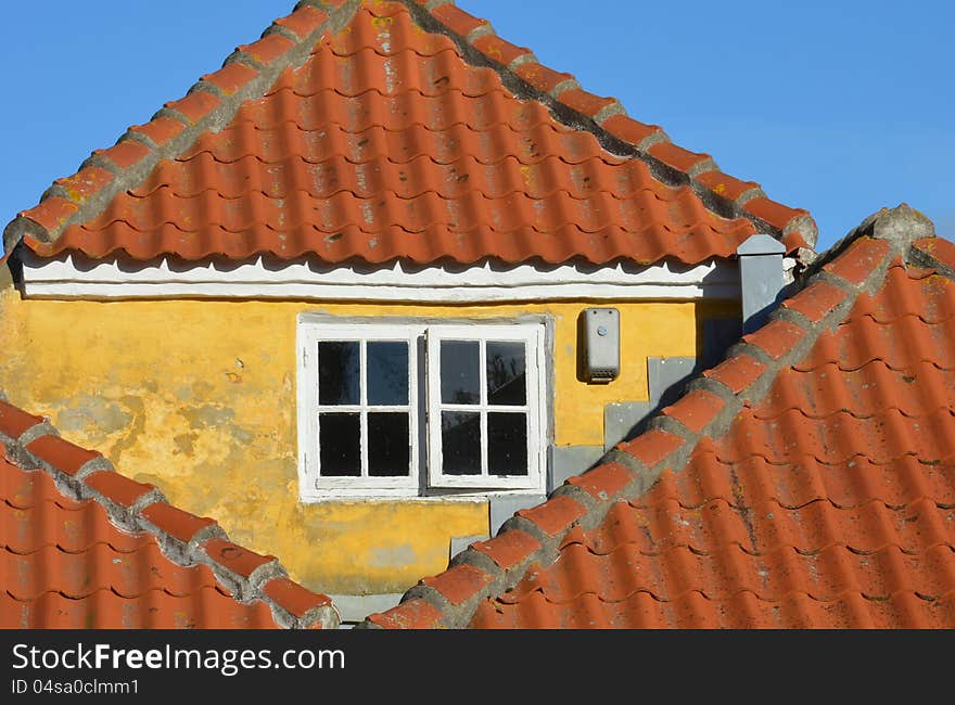 A triangular brick gable with yellow plaster and a white window is surrounded by triangular red tile roofs. A triangular brick gable with yellow plaster and a white window is surrounded by triangular red tile roofs