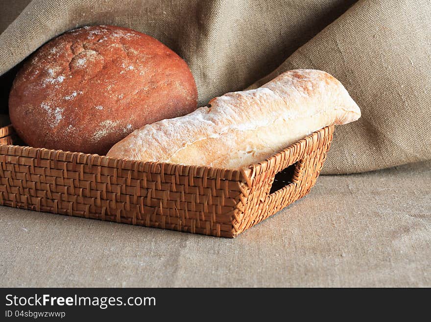 Nice wicker basket with rye and wheat bread on canvas background. Nice wicker basket with rye and wheat bread on canvas background