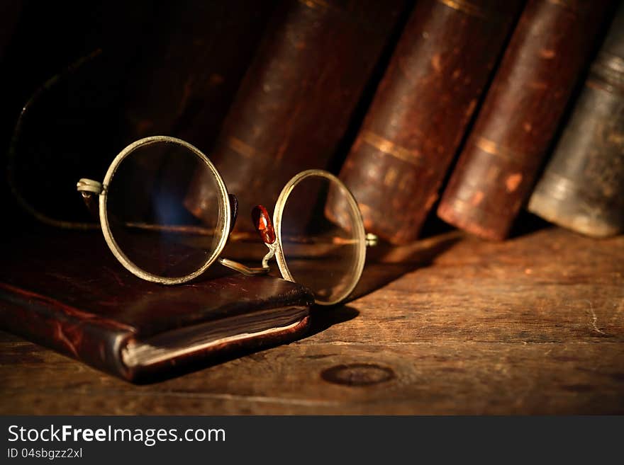 Old spectacles on leather notebook on background with old books