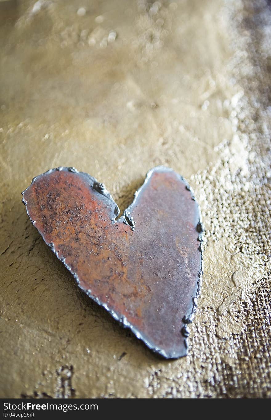 Handmade steel heart on golden hand painted burlap texture shot in natural light in a vertical format with copy space suitable for valentine. Handmade steel heart on golden hand painted burlap texture shot in natural light in a vertical format with copy space suitable for valentine