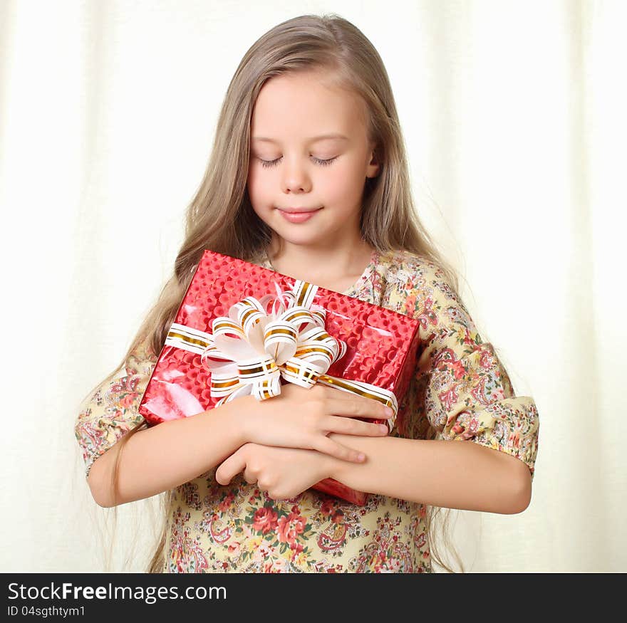 Little blond girl holding a red glamorous gift with pleasure