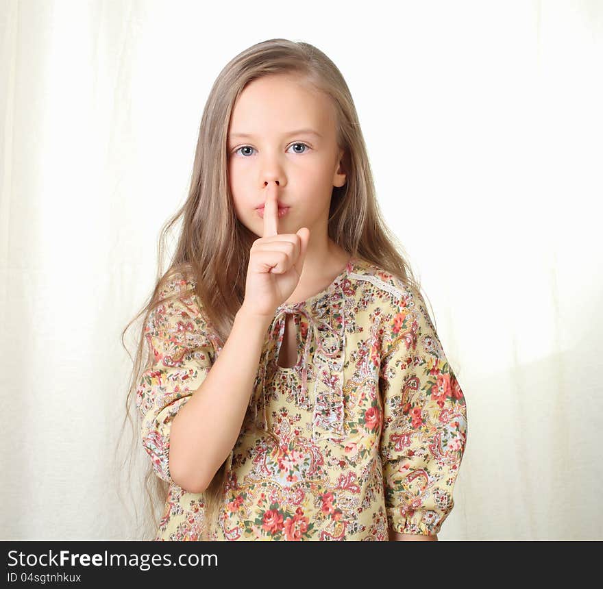 Little blond girl keepeing silence holding forefinger near lips