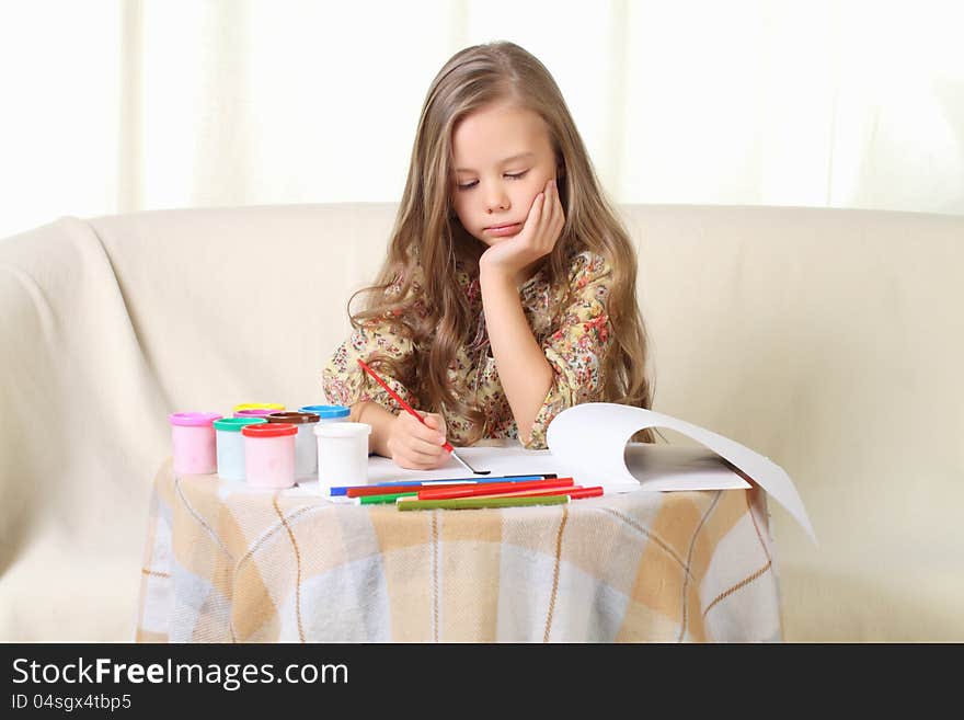 Little blond girl drawing at home on sofa