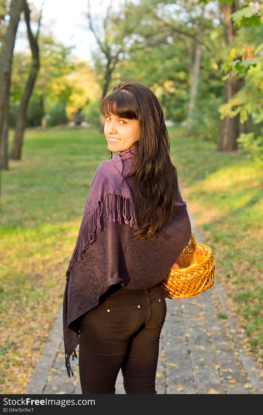 Beautiful woman carrying a basket walking through green countryside looking back over her shoulder with the sun in her face. Beautiful woman carrying a basket walking through green countryside looking back over her shoulder with the sun in her face