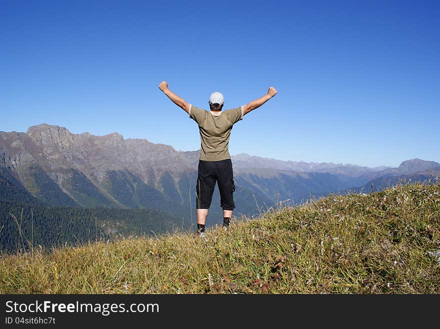 A man stands on a hillside with their hands up. A man stands on a hillside with their hands up