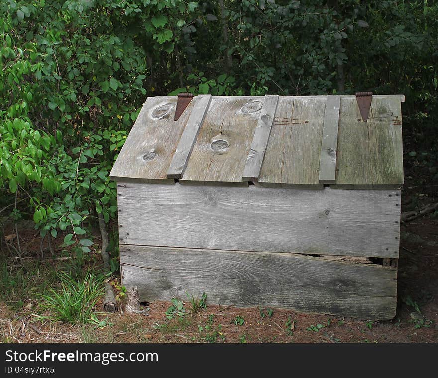 Old, weathered, and worn gray wooden outside storage box with hinged slanted lid, sitting in the bushes. Old, weathered, and worn gray wooden outside storage box with hinged slanted lid, sitting in the bushes.