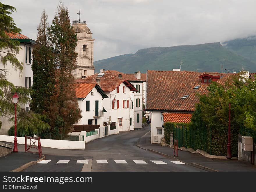 Typical basque village with a small churche in a center and historical white houses. The mountains in the clouds in the background. Typical basque village with a small churche in a center and historical white houses. The mountains in the clouds in the background.