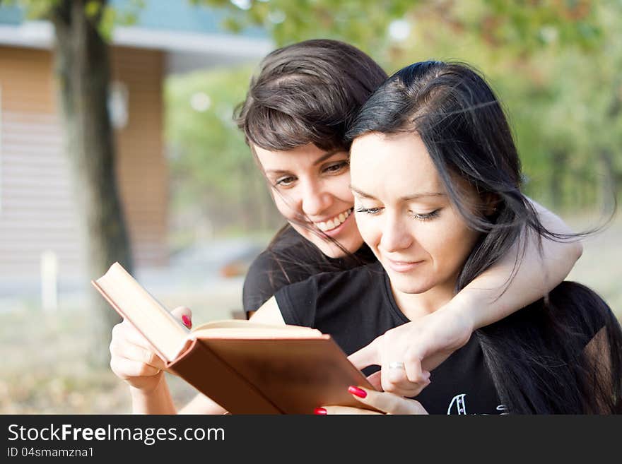 Two young women in a close embrace laughing together at the contents of a book. Two young women in a close embrace laughing together at the contents of a book