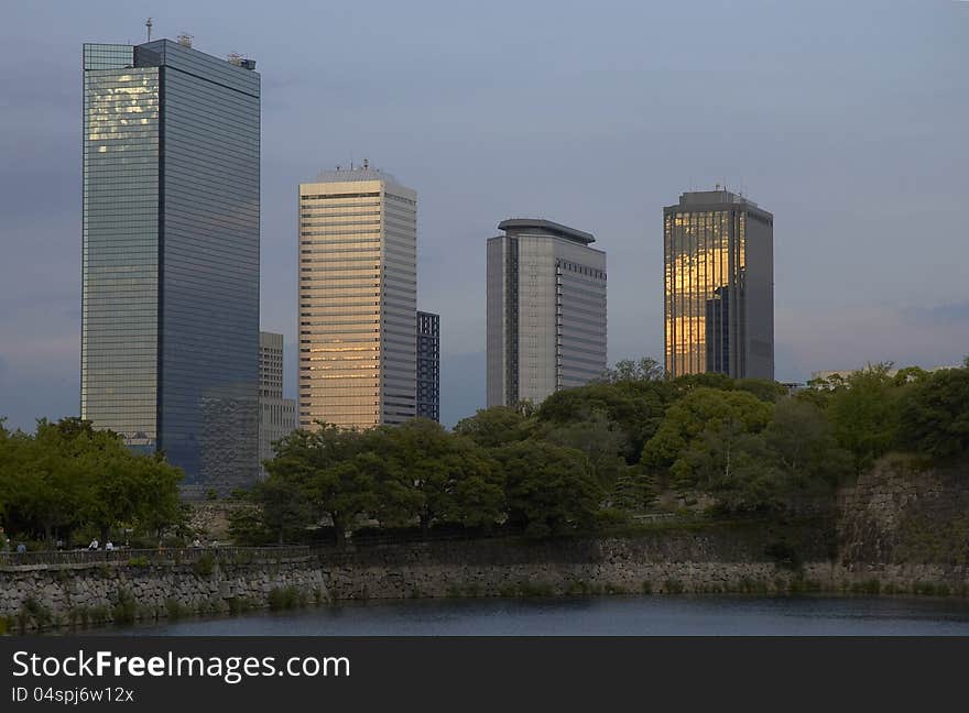 Skyscrapers with golden reflections at sunset behind a small forest with water