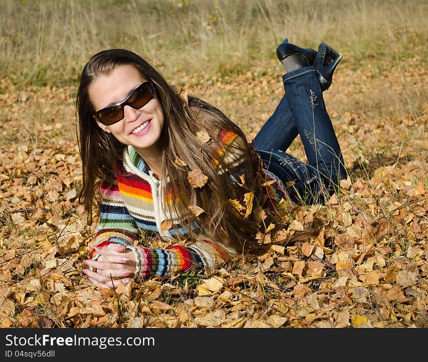 The beautiful smiling young woman lies on yellow autumn leaves. The beautiful smiling young woman lies on yellow autumn leaves