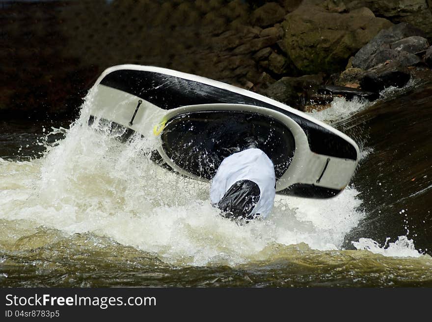 A black  kayak flips as a paddler does his stunts.