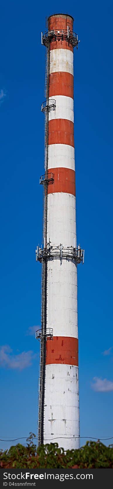 Industrial brick chimney with cellular equipment against blue sky