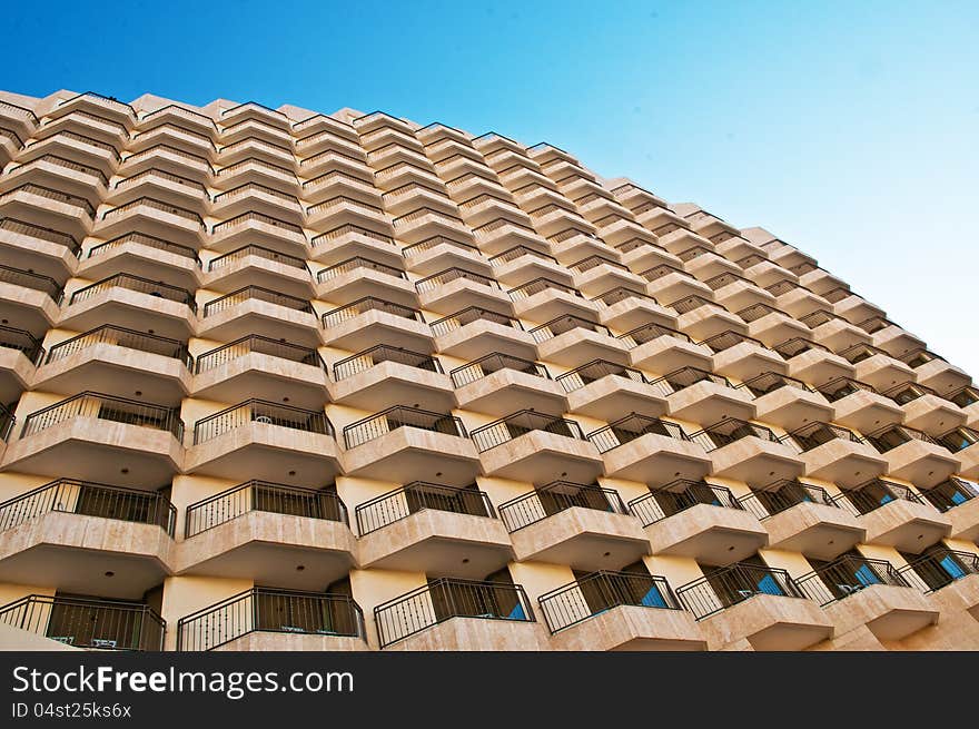 A fragment of a hotel balcony photographed from the bottom point against the blue sky. A fragment of a hotel balcony photographed from the bottom point against the blue sky