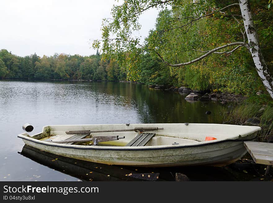 Old glass fiber boat on a lake coast in autumn colors. Old glass fiber boat on a lake coast in autumn colors