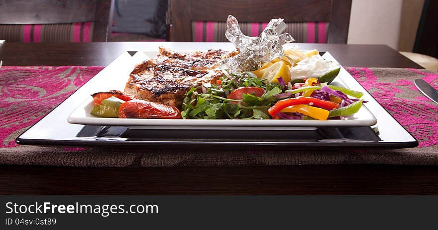 Grilled chicken on a white dish with vegetables on the background. Grilled chicken on a white dish with vegetables on the background.