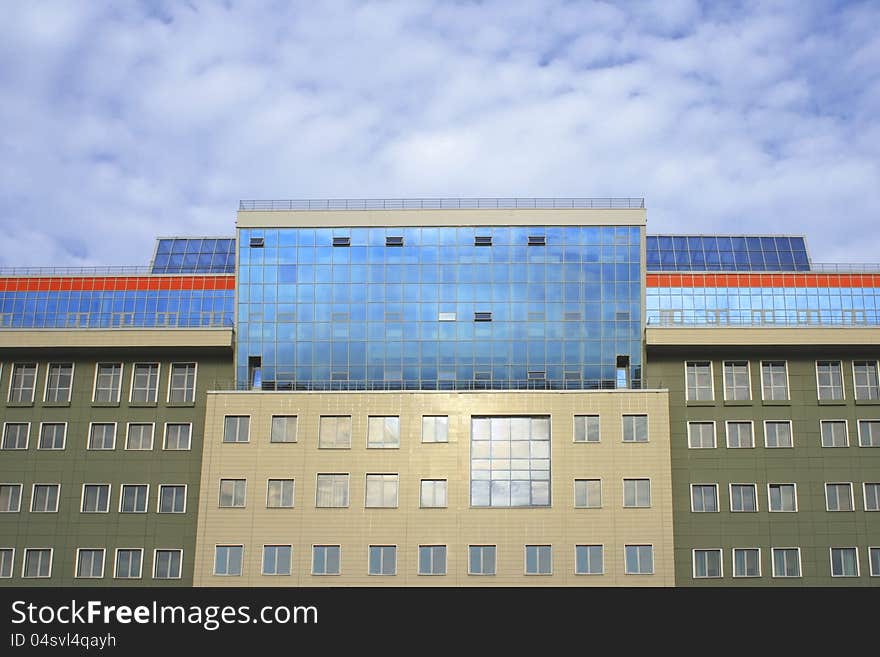 Photo of huge modern business and entertaining building with huge glass and bright orange strip against sky with clouds. Photo of huge modern business and entertaining building with huge glass and bright orange strip against sky with clouds