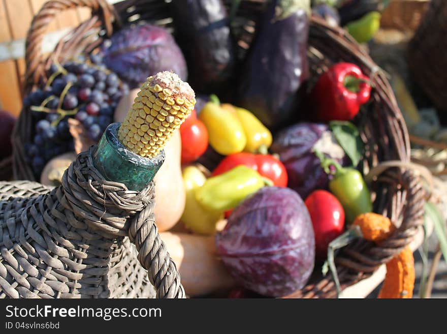 Demijohn with traditional cob stopper - corn cob and autumn vegetables exposed in the basket.