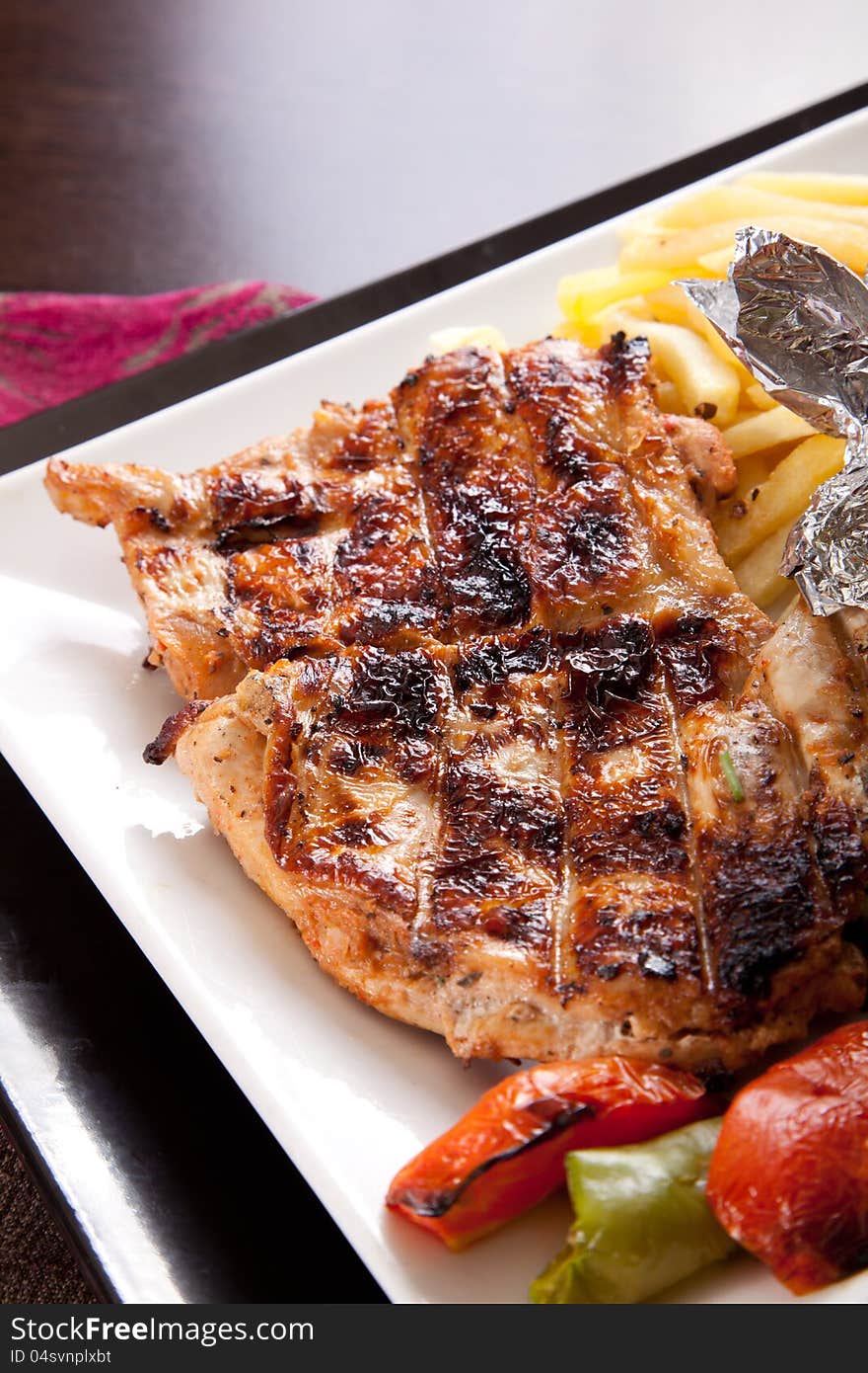 Grilled chicken on a white dish with vegetables on the background.