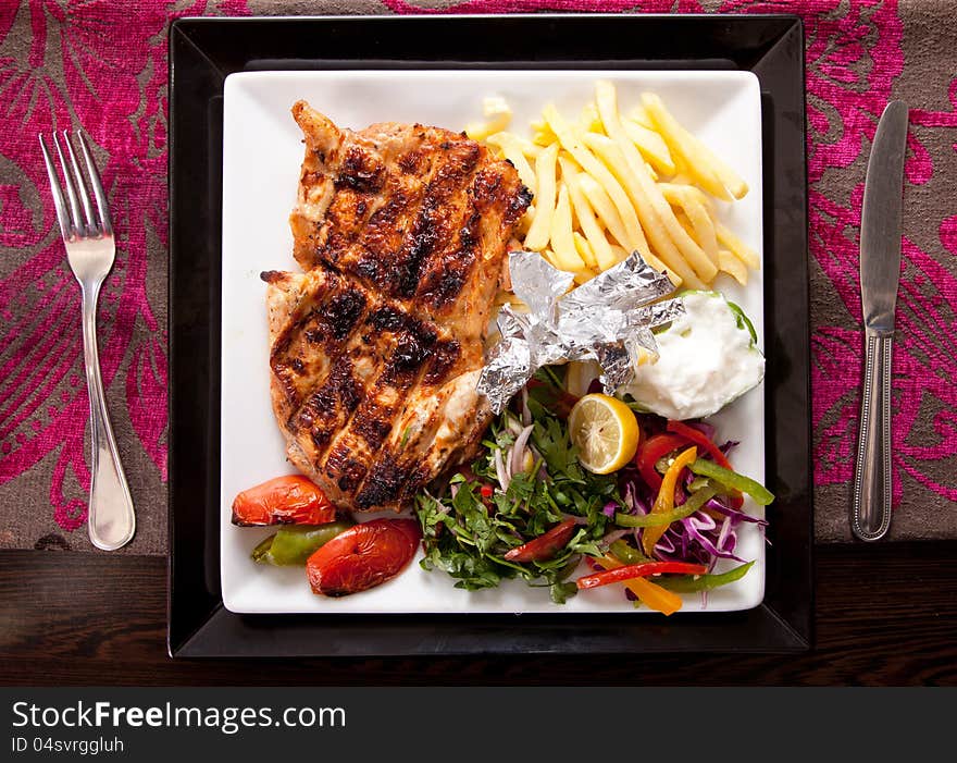 Grilled chicken on a white dish with vegetables on the background.