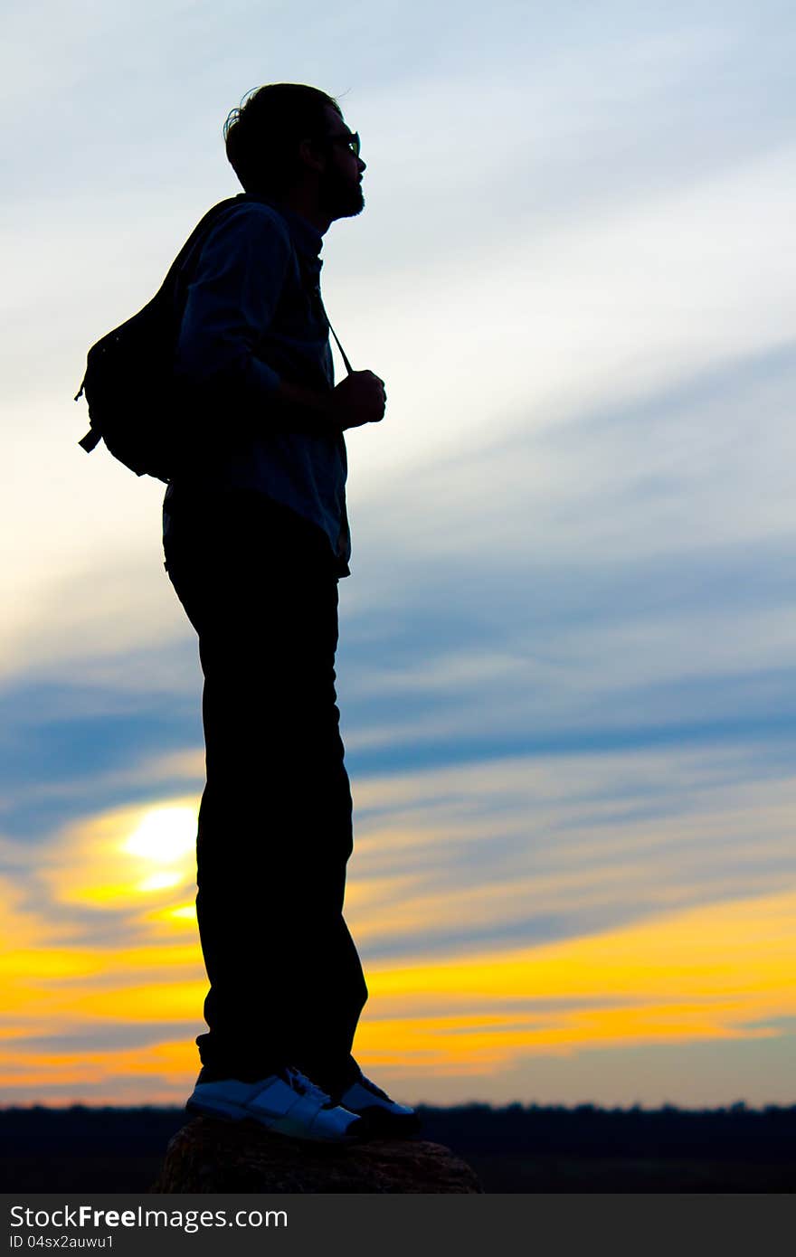 Silhouette of a man standing with a backpack or satchel on his back against a vivid orange sunset sky with copyspace. Silhouette of a man standing with a backpack or satchel on his back against a vivid orange sunset sky with copyspace