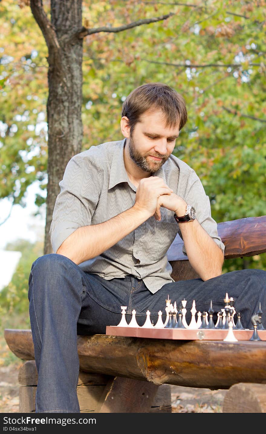 Low angle view ofa male chess player sitting on a wooden park bench contemplating the chessboard and working out his strategy. Low angle view ofa male chess player sitting on a wooden park bench contemplating the chessboard and working out his strategy
