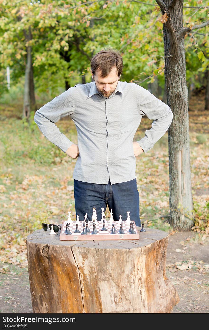 Man standing over a chessboard on a rustic log table in woodland planning his chess strategy. Man standing over a chessboard on a rustic log table in woodland planning his chess strategy