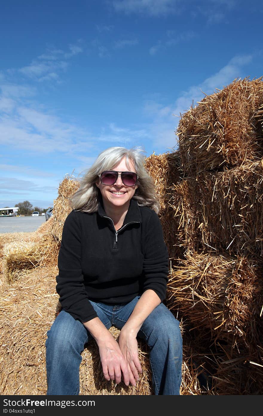 Attractive middle aged woman sits enjoying the sun on straw bales on a beautiful fall day. Attractive middle aged woman sits enjoying the sun on straw bales on a beautiful fall day.