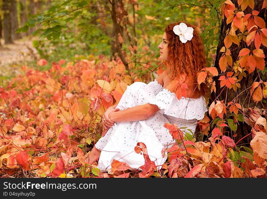 Beautiful red-haired young woman, wearing in white dress or the bride and decoration in form of flower on her head among red leaves in autumn forest.and dreaming. symbol of autumn. Beautiful red-haired young woman, wearing in white dress or the bride and decoration in form of flower on her head among red leaves in autumn forest.and dreaming. symbol of autumn