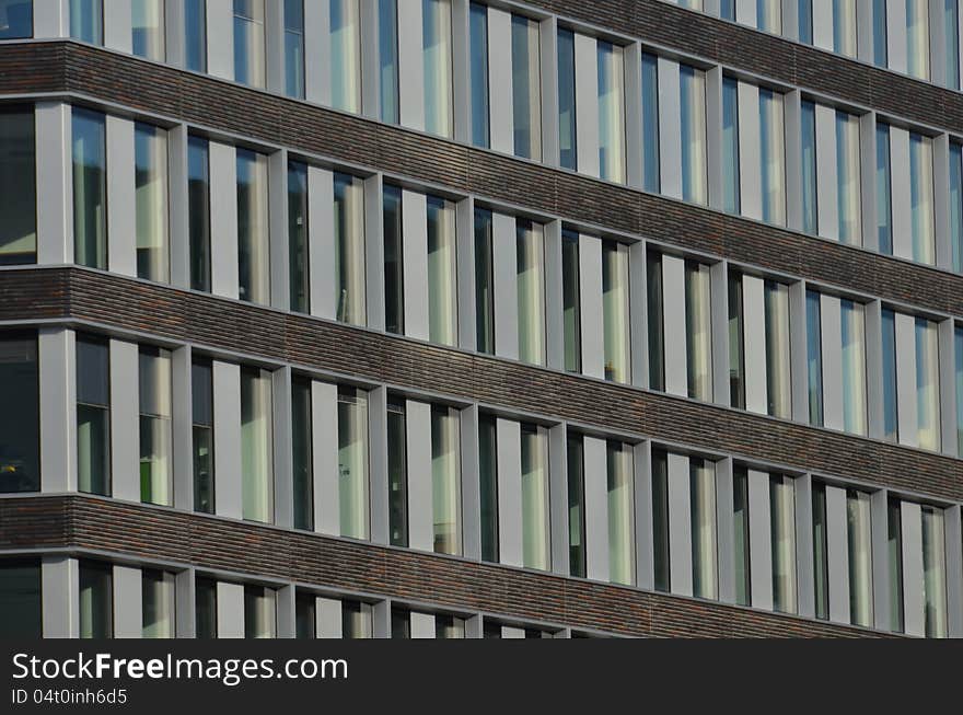 The facade of a modern office building with vertical white panels and horizontal red brown brick stripes