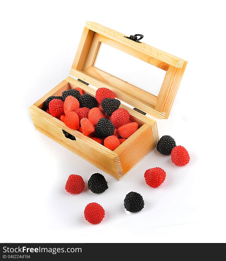 A wooden box with candies of black and red colors isolated on a white background. Some candies are outside the box. A wooden box with candies of black and red colors isolated on a white background. Some candies are outside the box.