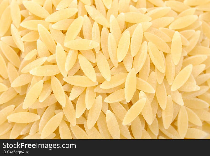 A close-up shot of rice-shaped orzo (risoni) pasta as a background. A close-up shot of rice-shaped orzo (risoni) pasta as a background