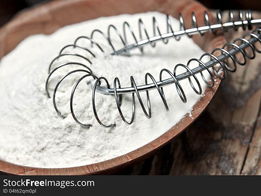 Wheat flour and whisk on wooden background