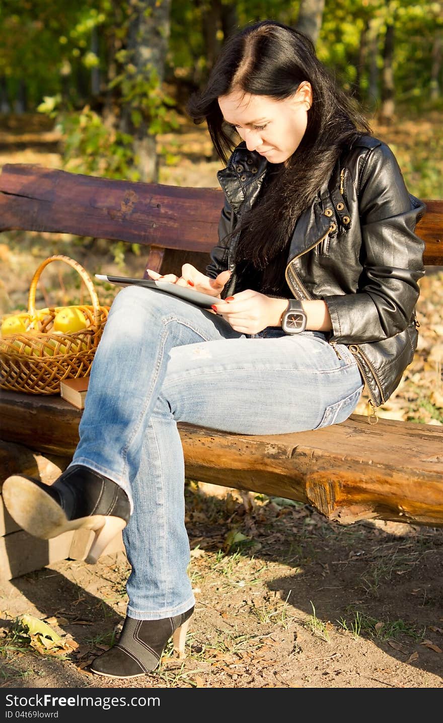 Woman sitting on a wooden bench in the country with a basket of apples using her tablet. Woman sitting on a wooden bench in the country with a basket of apples using her tablet