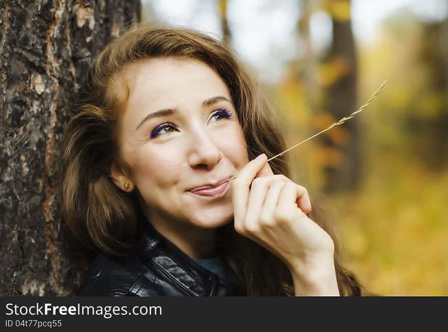 Portrait of smiling girl sitting near the tree in red autumn forest